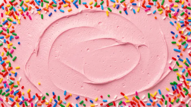 Smooth swirled pink frosting backdrop lined with rainbow sprinkles along its edges, with an empty copy space center