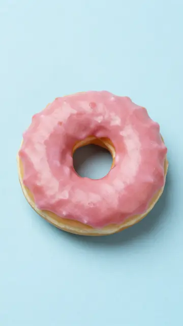 A ring donut with soft pink icing sits centered on a smooth pastel blue background