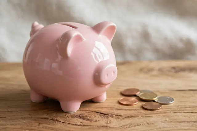 Glossy pink ceramic piggy bank rests on a wooden table next to scattered coins.