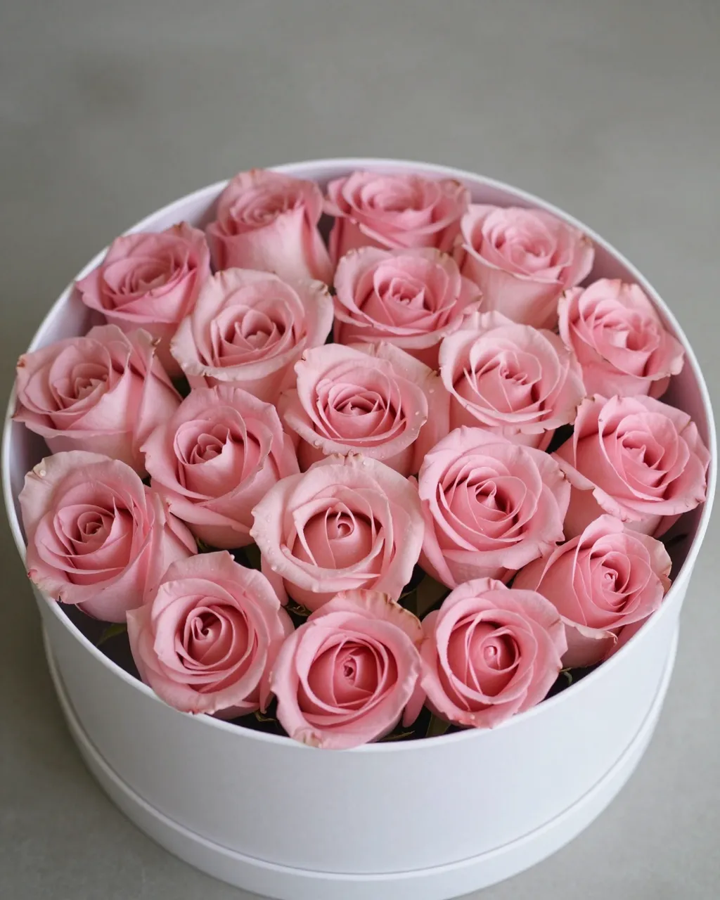 Top view of a round white hatbox filled with soft pink roses resting on a neutral gray surface