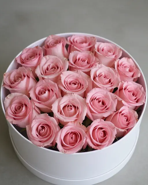 Top view of a round white hatbox filled with soft pink roses resting on a neutral gray surface