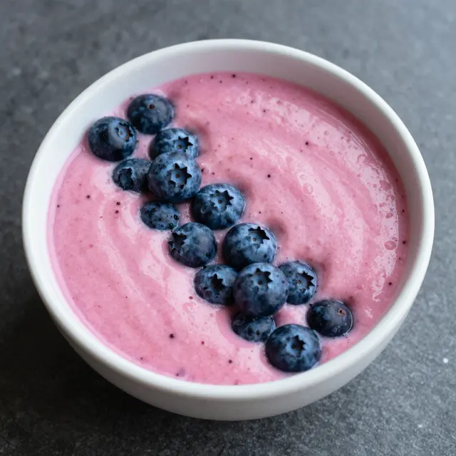 Top view of a white bowl filled with pink dragon fruit smoothie topped with fresh blueberries on a dark gray countertop