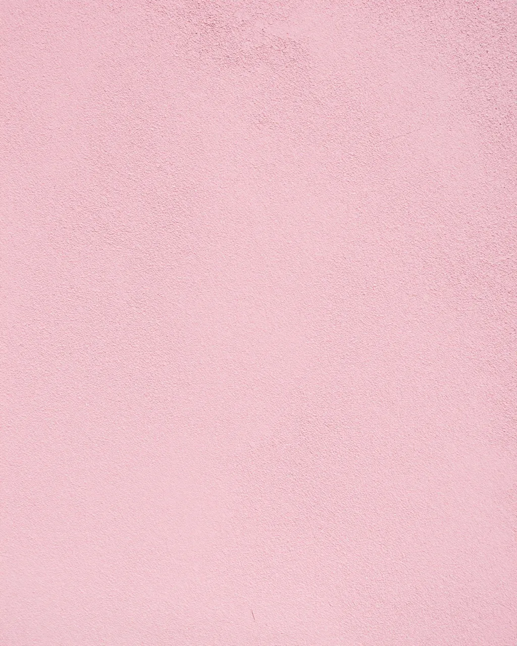 Full frame close-up of a rough sandy finish pink stucco wall in bright even light