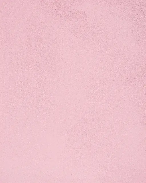 Full frame close-up of a rough sandy finish pink stucco wall in bright even light
