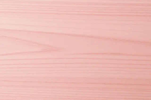 Full frame close-up of smooth pink toned beech wood with fine horizontal grain patterns under flat even light