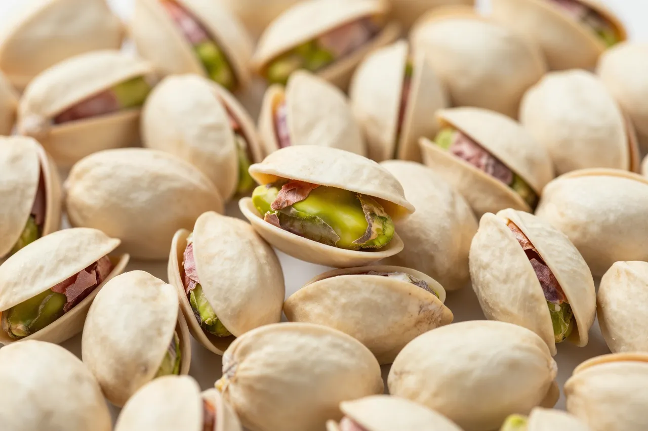 Dense close-up of shelled pistachios, many partially opened to show green nut kernels, filling the entire frame