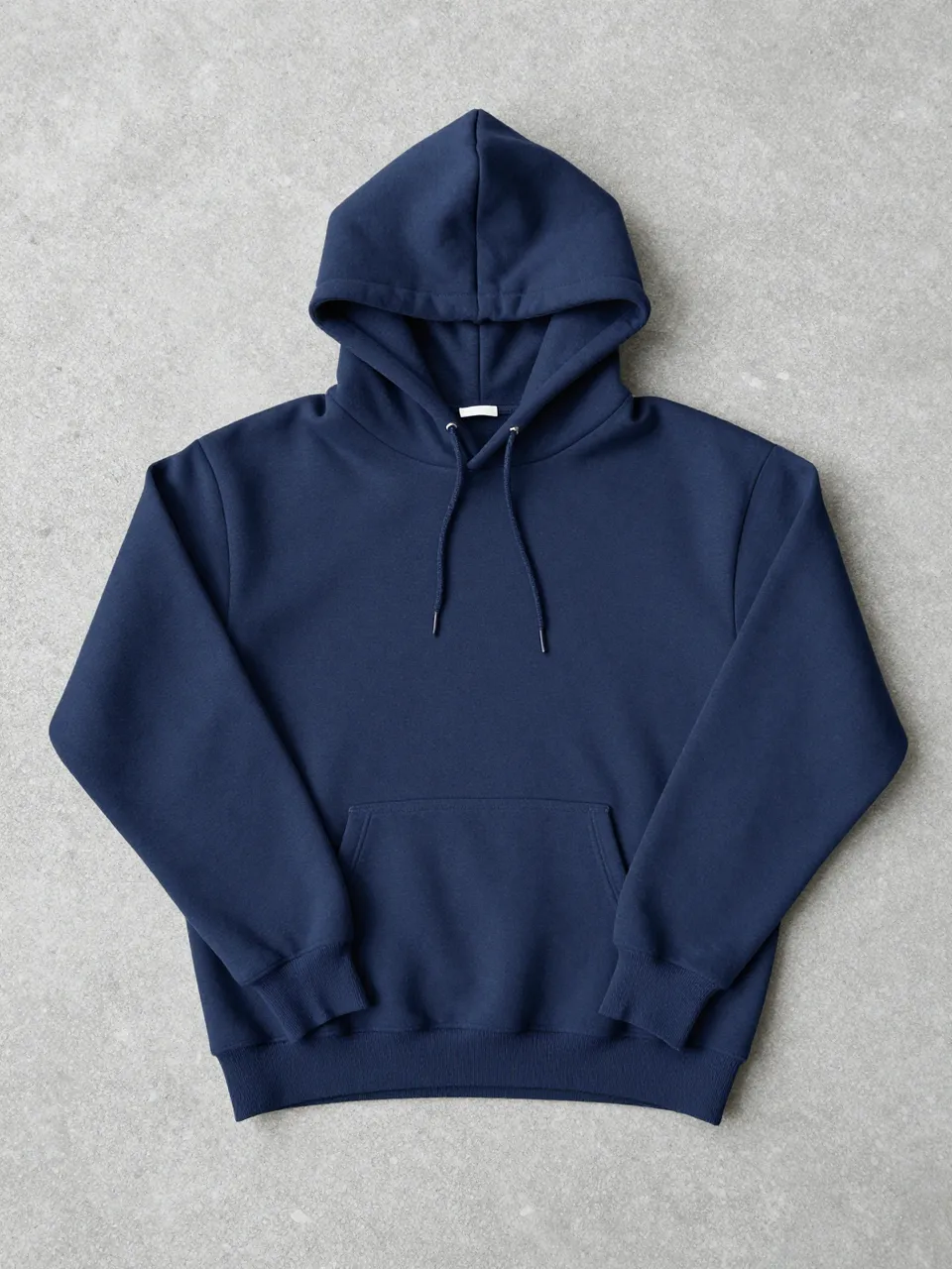 A flat-lay plain navy hoodie rests spread out on a smooth gray concrete surface.
