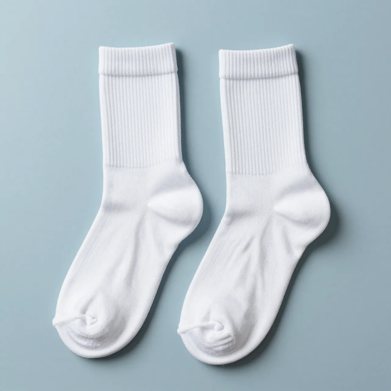 Pair of plain white ribbed crew socks laid flat on a pale blue matte surface