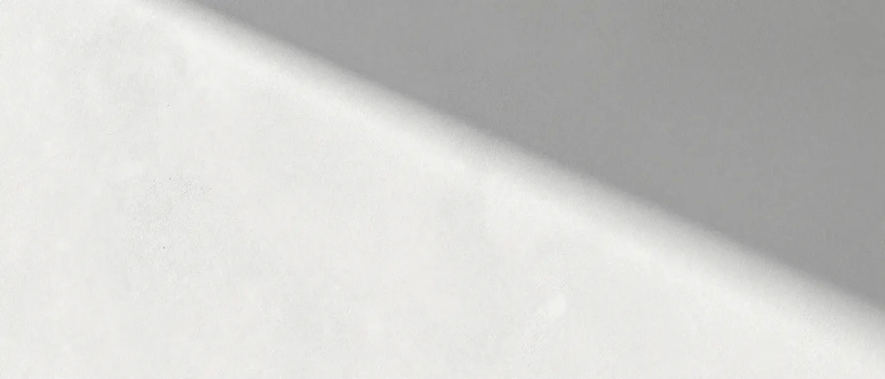 A rough white plaster wall with a soft diagonal sunbeam stretching across the frame