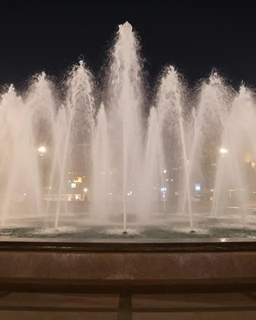 Long exposure shot of a stone plaza fountain with misty water jets against a dark night sky
