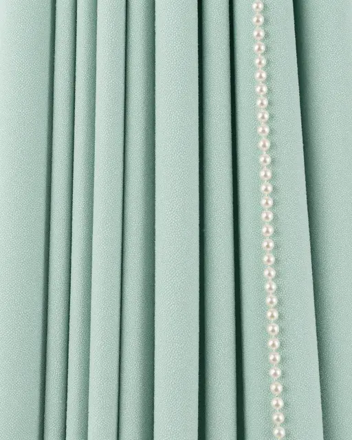 Full frame close-up of pleated pale mint shagreen surface paired with a straight strand of small glossy pearls