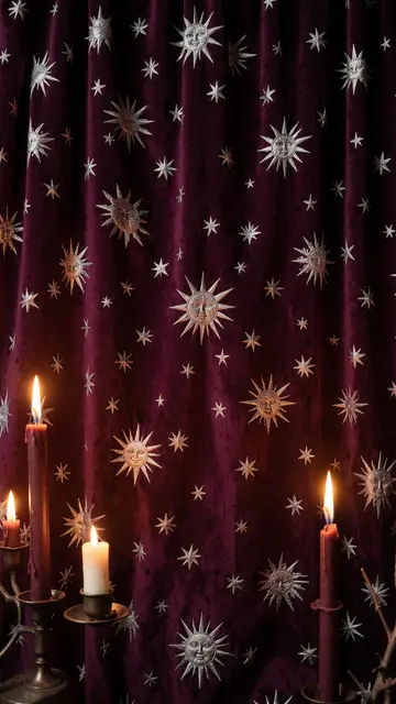 Lit candles sit in front of a deep plum velvet curtain embroidered with silver suns and stars