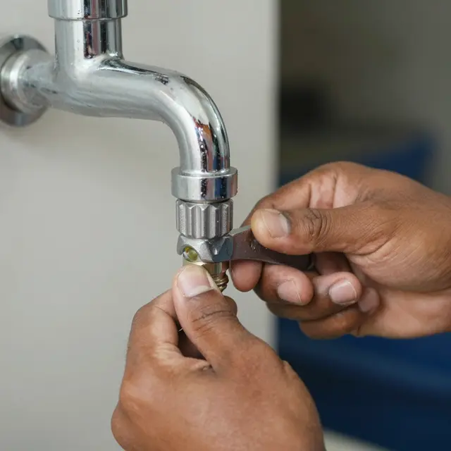 Close-up of a Pacific Islander plumber's hands using a wrench to tighten a chrome faucet fitting.