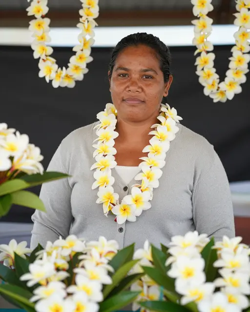 Pacific Islander woman stands behind her flower stall surrounded by fresh plumeria leis