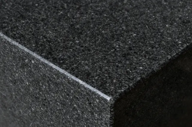 Close-up of the sharp corner edge of a polished black granite slab with fine sparkling flecks