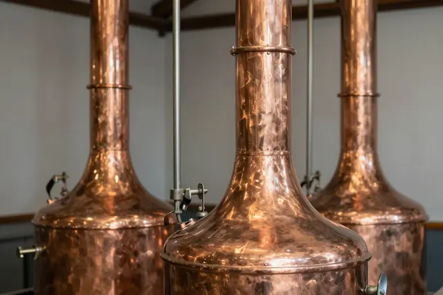 Three hammered polished copper brewing kettles stand in a quiet warm-lit brewhouse interior