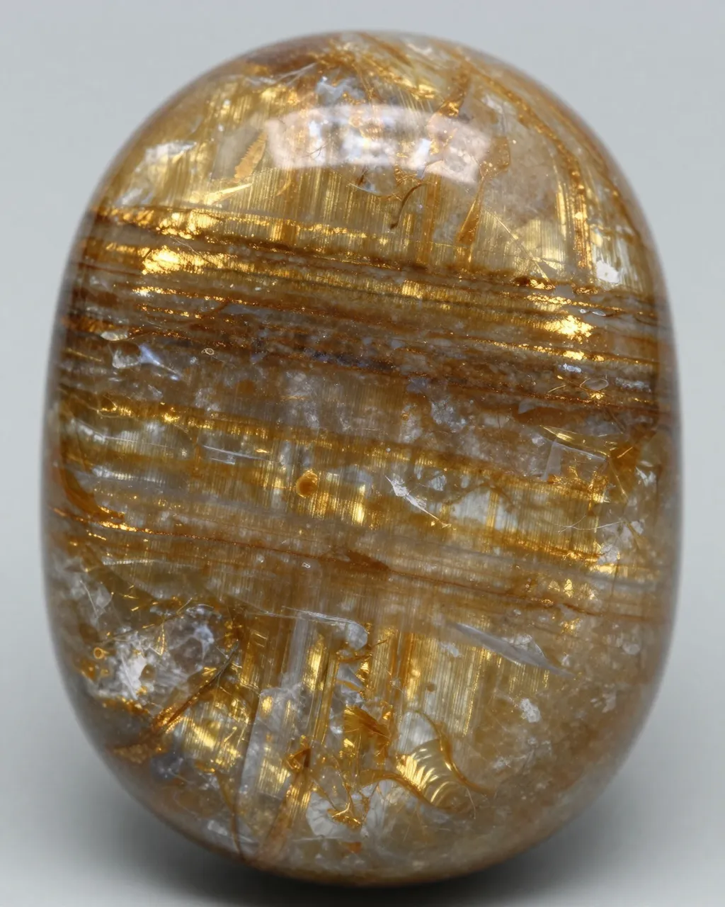 Close-up of a polished oval chatoyant quartz crystal with shimmering golden-brown banded inclusions