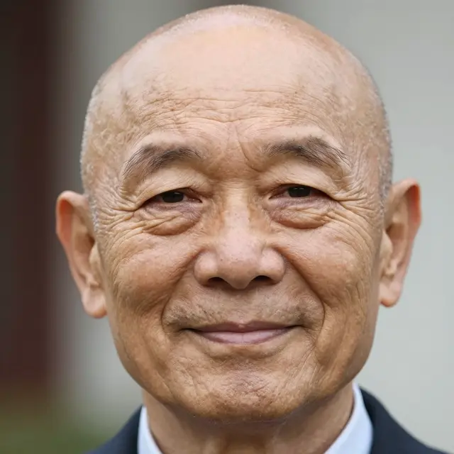 Close-up portrait of a bald elderly East Asian man with a gentle warm smile.