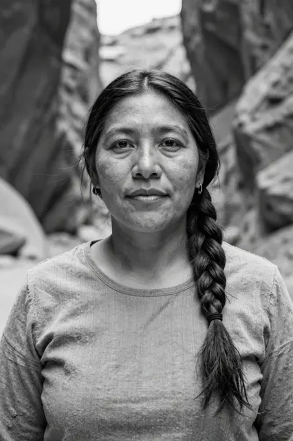 Black and white portrait of an Indigenous woman in her forties with a long braid, standing in a rocky canyon