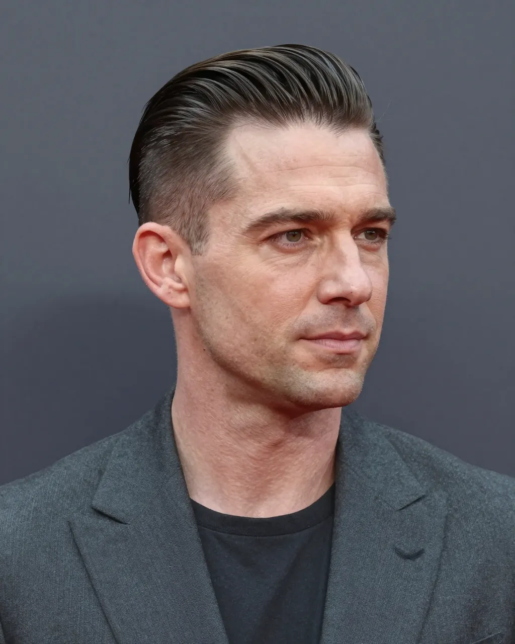 Head and shoulder portrait of a forties man with slicked undercut hair against a dark grey backdrop