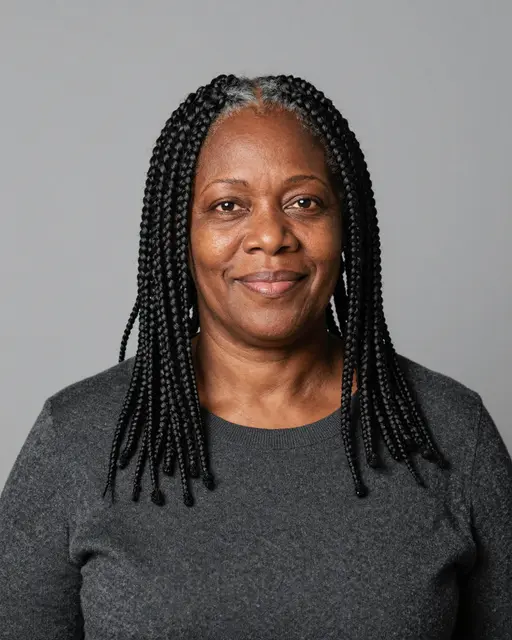 Studio portrait of a Black woman in her fifties with box braids, wearing a charcoal sweater and smiling gently against a