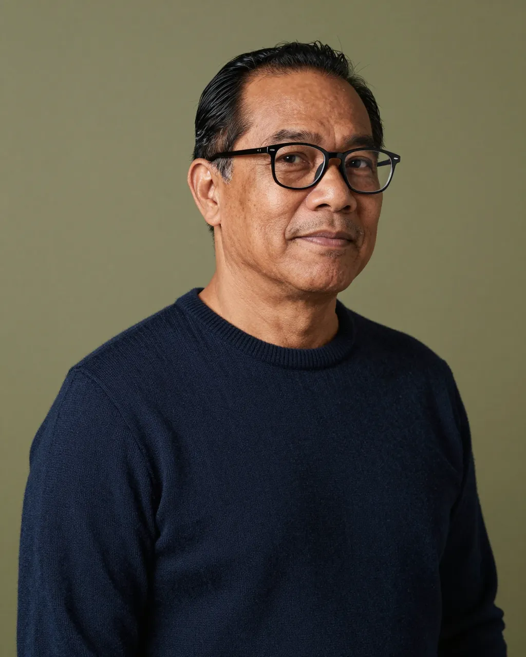 Headshot of a fifties Pacific Islander man in glasses and a navy sweater against an olive green backdrop