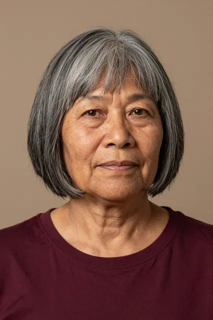 Studio portrait of an older woman with grey bobbed hair wearing a burgundy top against a neutral tan background