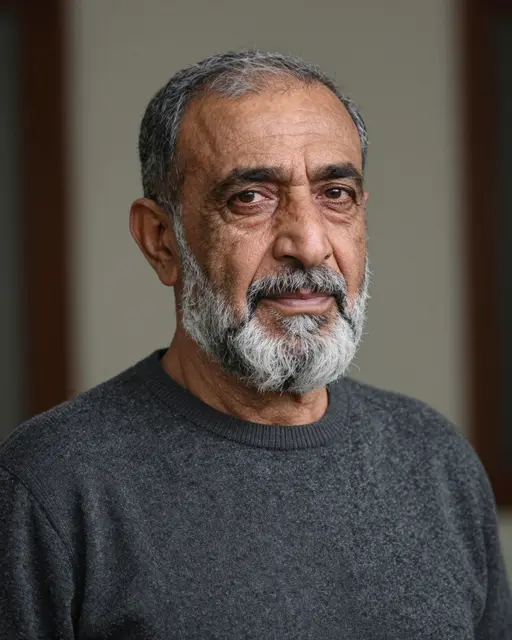 Close-up portrait of a senior Middle Eastern man with a gray beard wearing a dark sweater, looking calmly at the camera
