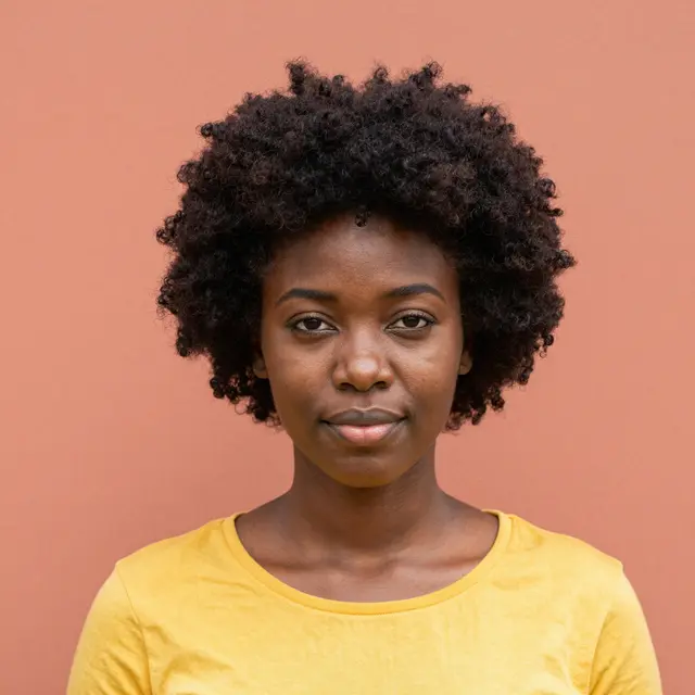 A Black woman in her late twenties with curly afro hair and a plain yellow top looks directly at the camera against a smooth