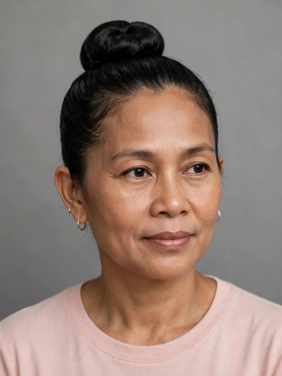 Headshot portrait of a middle aged Southeast Asian woman with a neat high bun against a plain grey backdrop
