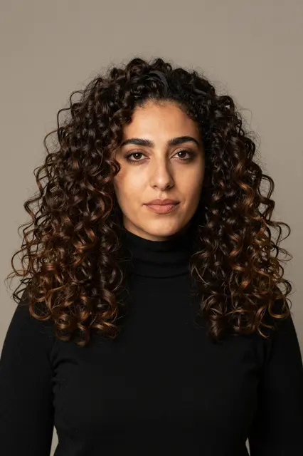 Studio portrait of a Middle Eastern woman in a black turtleneck facing the camera against a warm grey backdrop