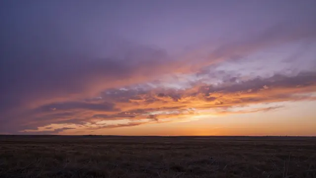 Purple and orange sunset clouds stretch above a wide flat grass prairie horizon
