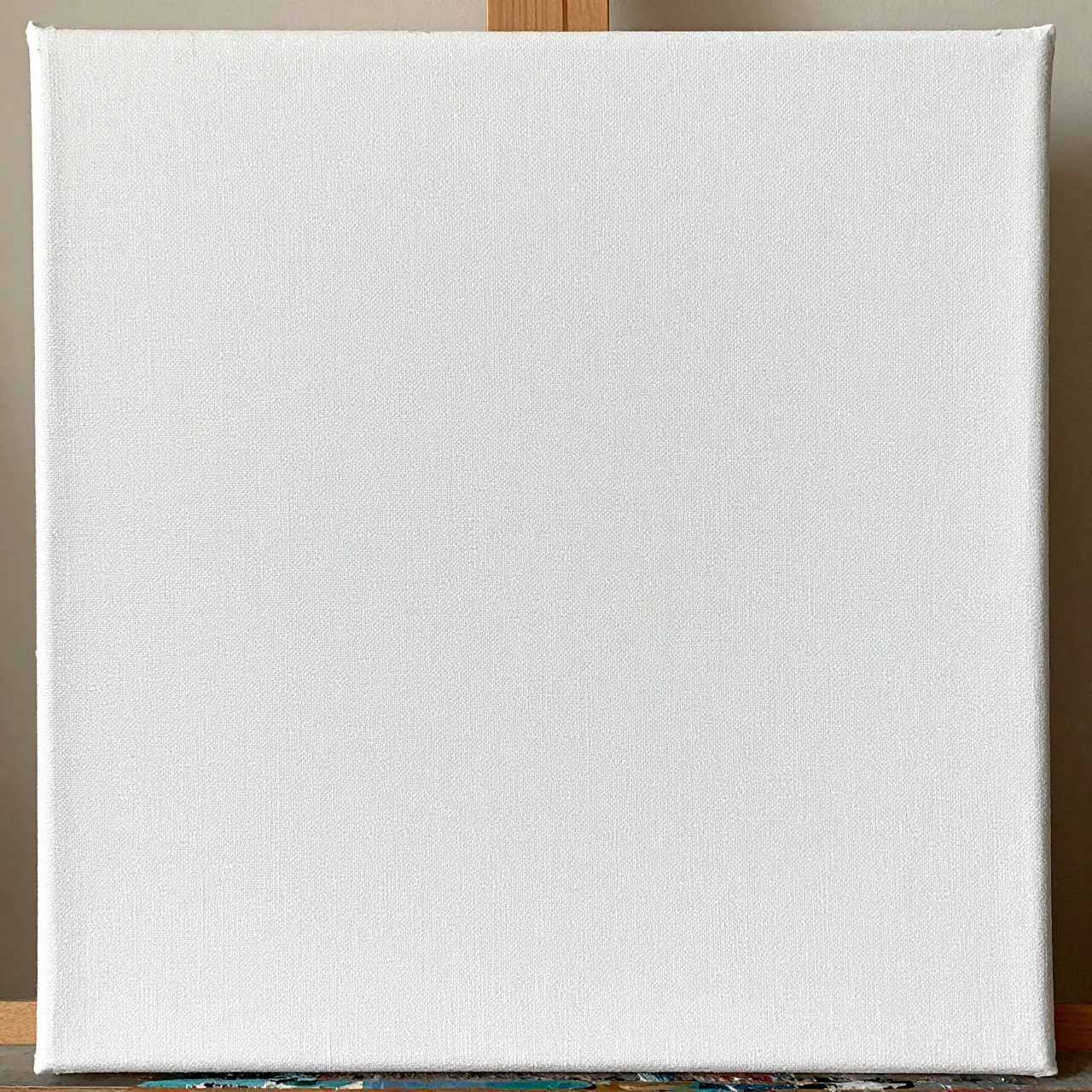 A close-up of a plain gesso-primed white stretched canvas resting on a wooden easel