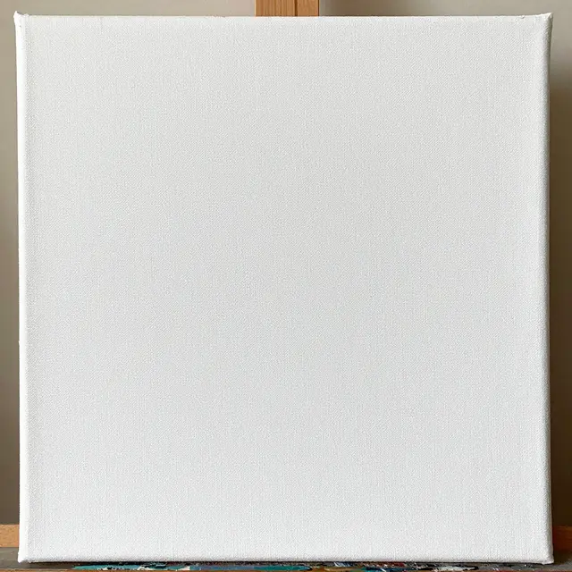A close-up of a plain gesso-primed white stretched canvas resting on a wooden easel