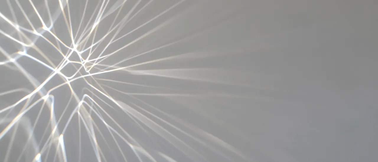 Glowing thin prismatic light lines spread from the left edge across a pale gray background with empty right side copy space