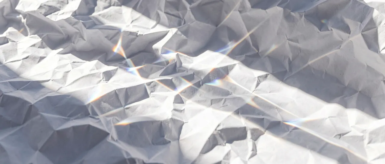 Bright sunlight casts rainbow prismatic light refractions across crumpled white paper