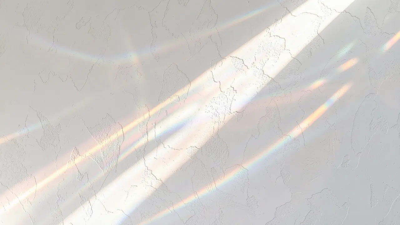 Rainbow prismatic light beams drift diagonally across a textured white plaster wall