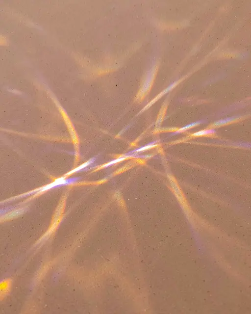 Iridescent gold and violet prismatic light streaks spread across a smooth sand-toned matte surface