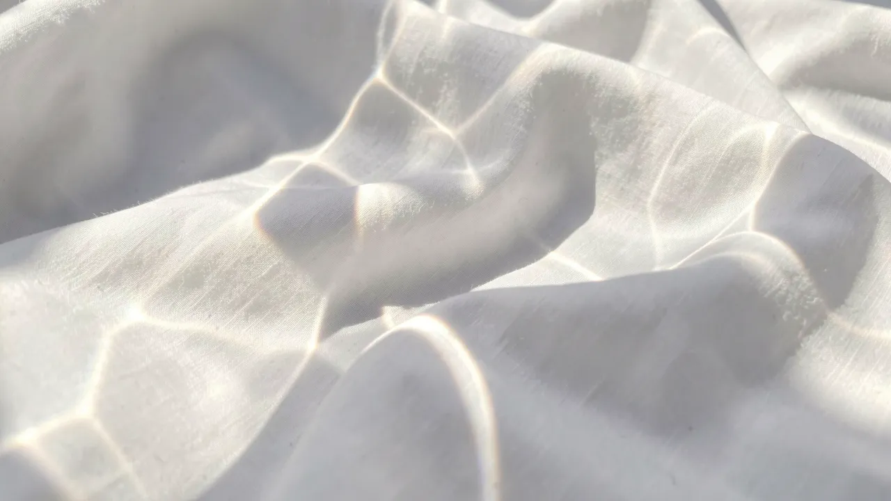 Prismatic sun caustics drift across soft folded crisp white fabric in bright morning light