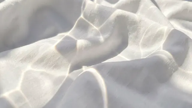 Prismatic sun caustics drift across soft folded crisp white fabric in bright morning light
