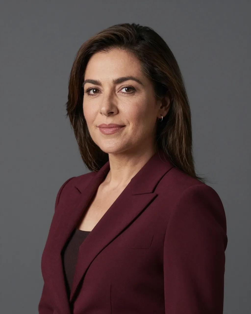 Studio portrait of a Latina woman in a burgundy blazer against a charcoal gray backdrop