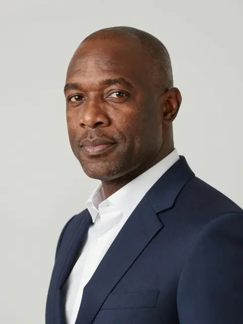 Three-quarter headshot of a middle aged Black man in a navy suit against a light gray backdrop