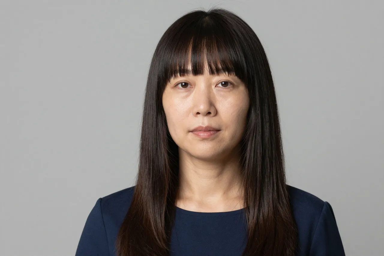 Headshot of a forties East Asian woman with blunt bangs and long sleek hair against a soft grey backdrop
