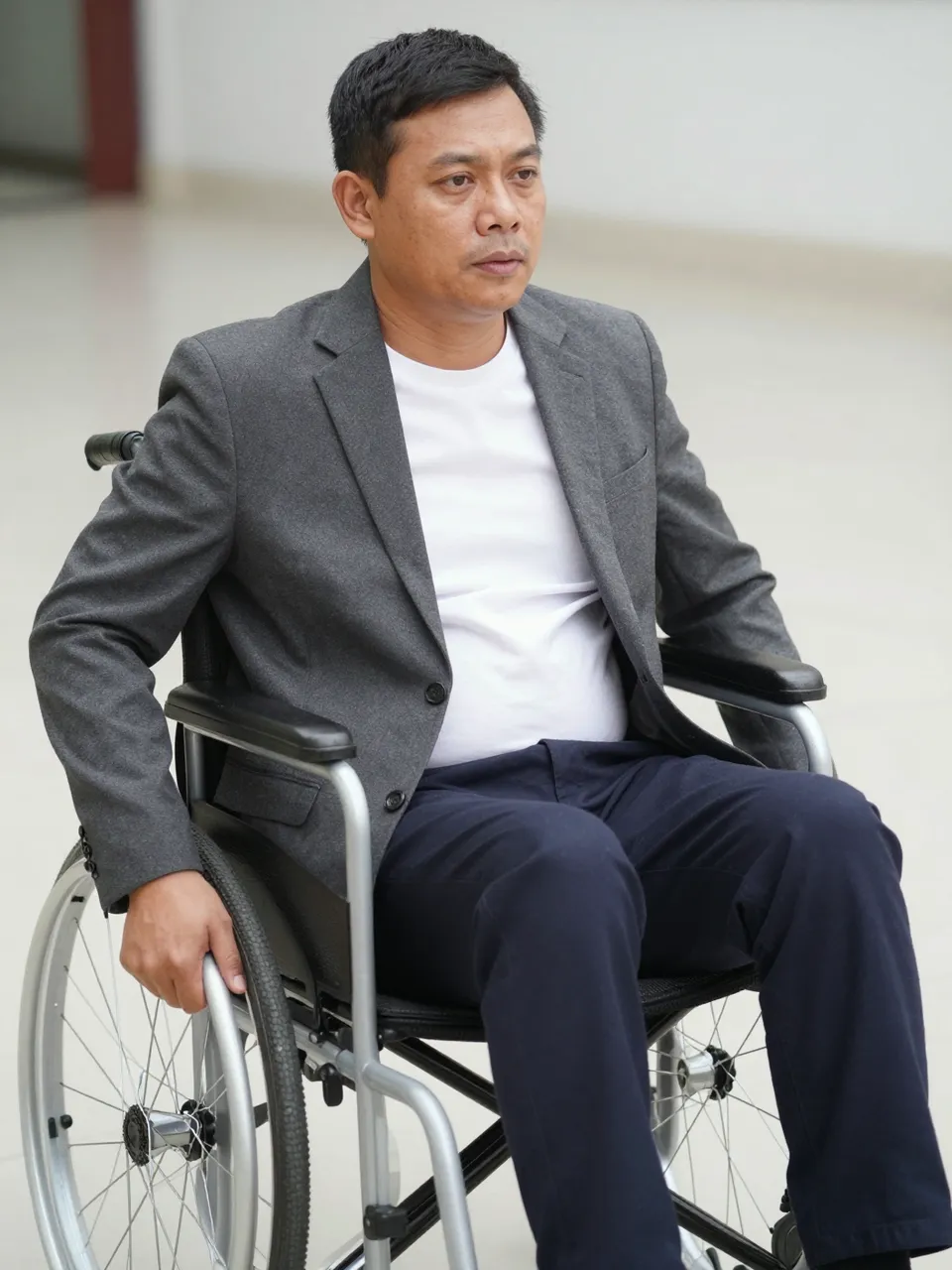 Southeast Asian man in business casual work attire sitting in a wheelchair indoors