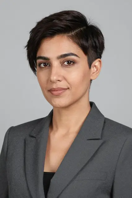 Headshot portrait of a Middle Eastern woman in a charcoal blazer against a soft grey backdrop