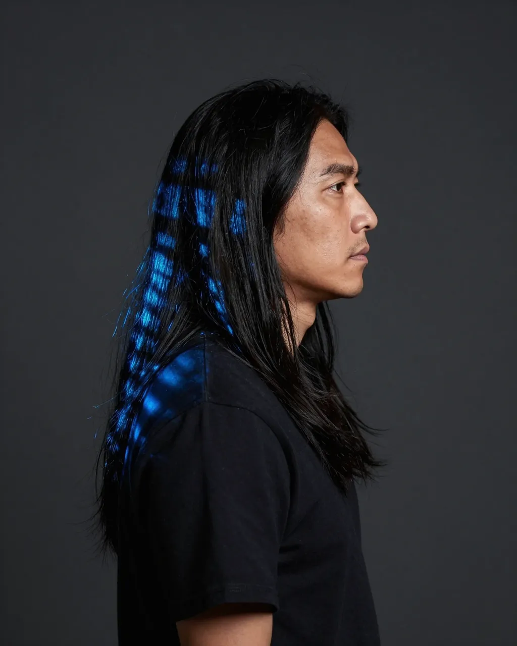 Side profile studio portrait of a man with long black hair lit by projected blue grid light