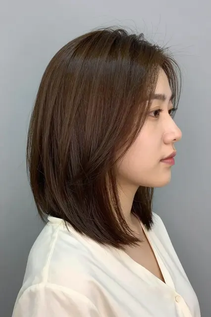 Profile portrait of an East Asian woman in her thirties with a glossy chin-length bob against a soft grey background