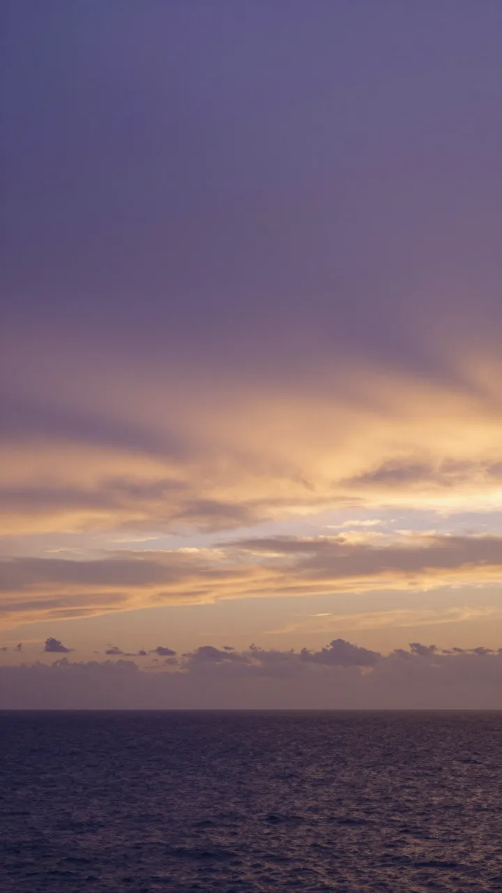 Vertical view of a calm ocean beneath a purple and warm gold sunset sky with layered clouds