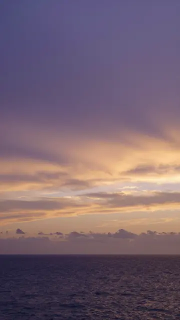 Vertical view of a calm ocean beneath a purple and warm gold sunset sky with layered clouds