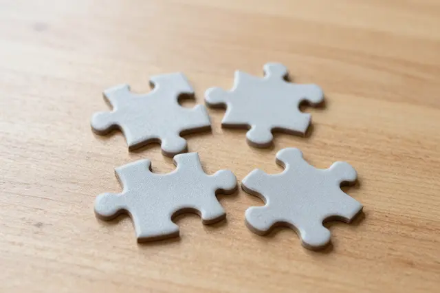 Four plain gray jigsaw pieces rest loosely arranged on a light brown wooden tabletop.